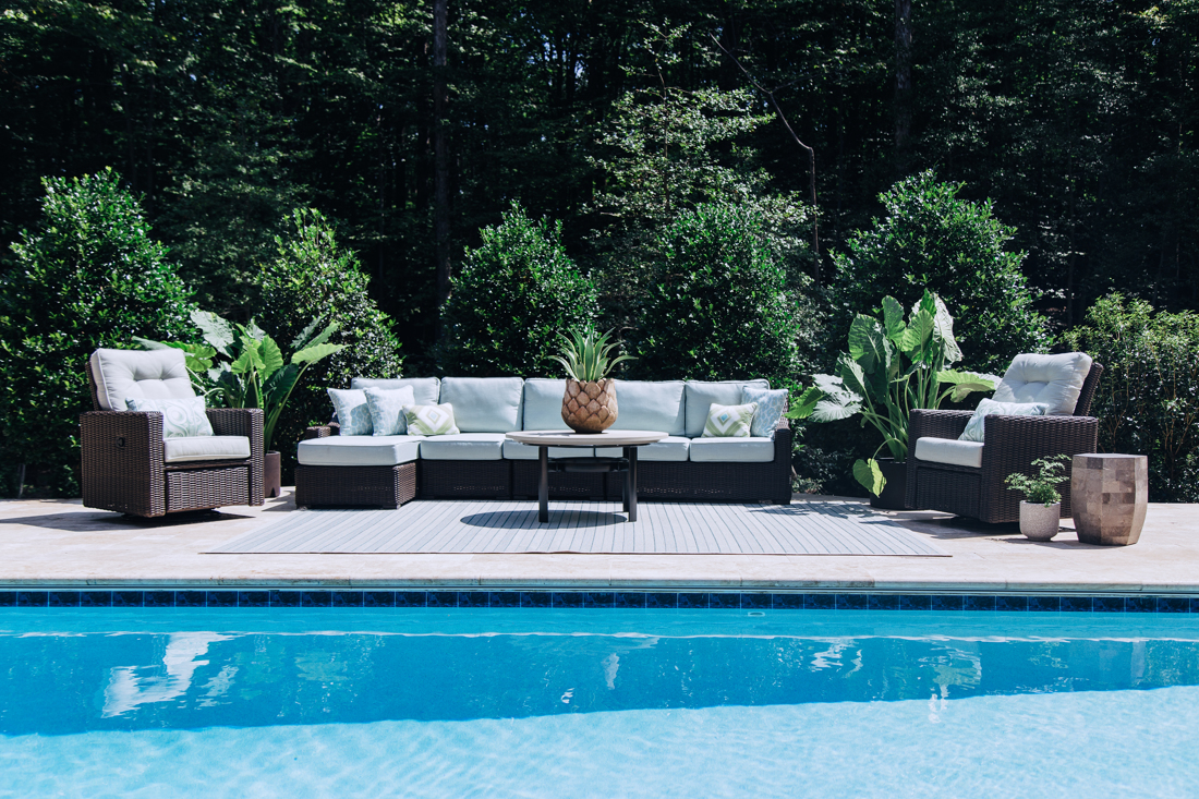 Poolside lounge seating with soft blue cushions framed by layered greenery, styled by The Open Door Style & Design