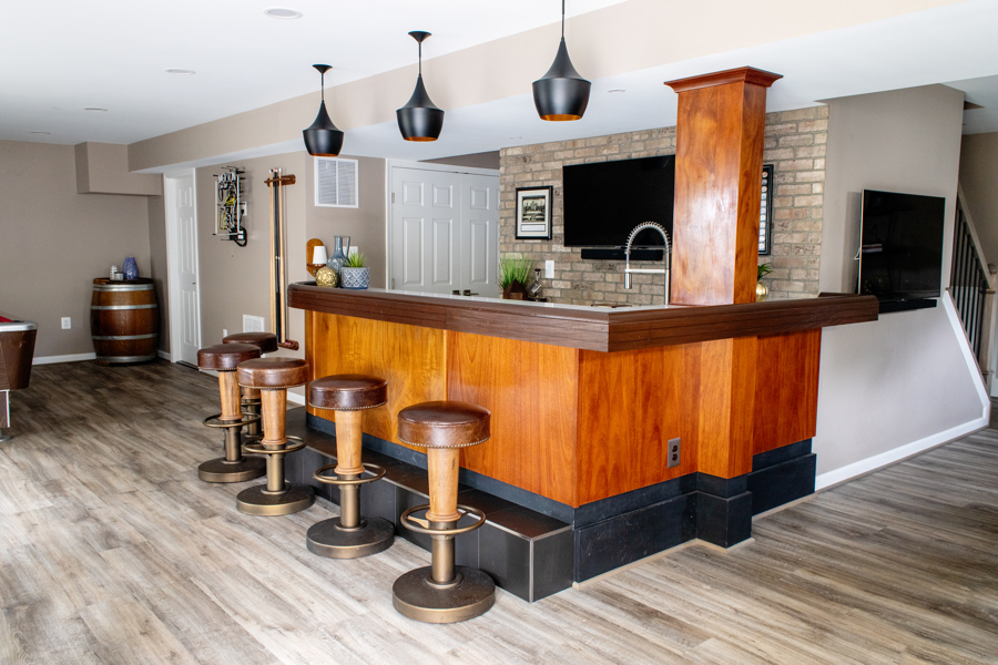 Finished basement bar with warm wood, exposed brick, and navy built-ins