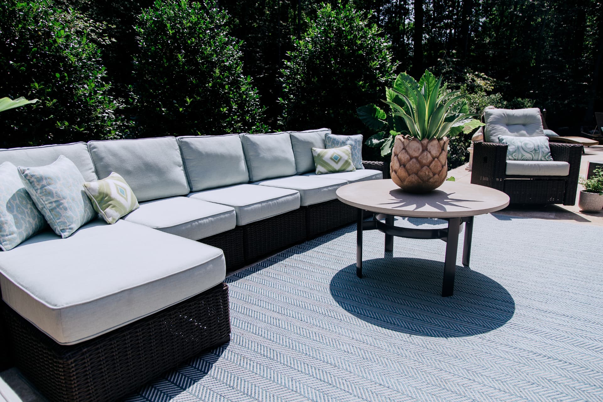 Outdoor sectional with patterned pillows and a pineapple planter on a woven area rug